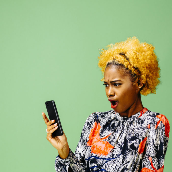 Woman looking at her phone with mouth wide open, isolated on green studio background